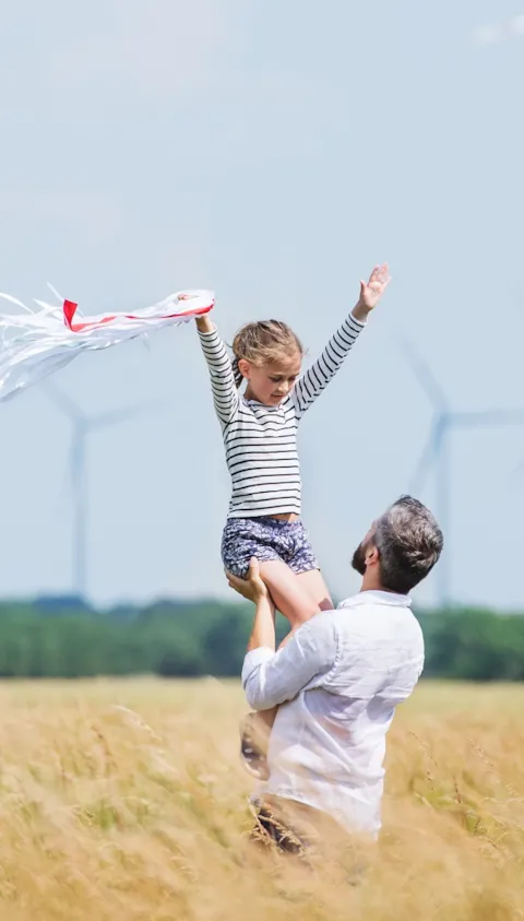 Mature father with small daughter standing on field on wind farm